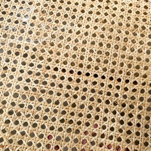 May include: Close-up of a woven rattan material with a repeating pattern of small, evenly spaced holes. The natural, light brown material is tightly woven, creating a textured surface. This material is often used for furniture and decorative items.