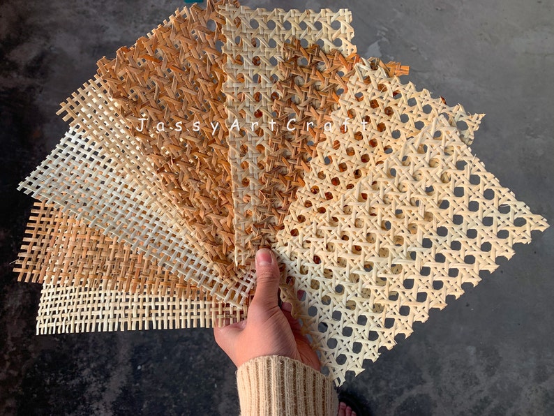 May include: A hand holds a fan of woven rattan sheets in varying shades of beige and brown. The sheets have a geometric pattern and are labeled "Jassy Art Craft".