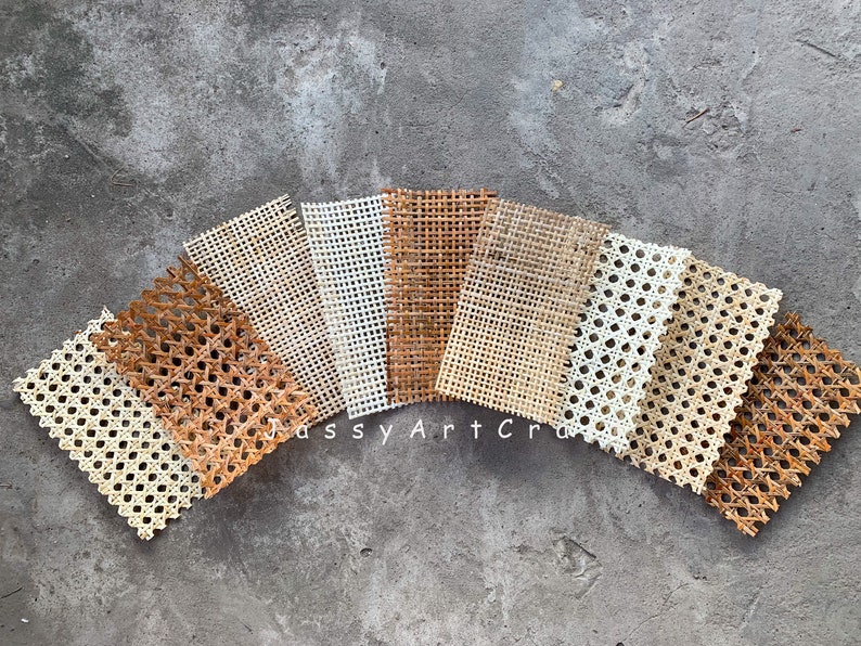 May include: Assortment of woven cane webbing samples in various natural tones, including light beige, medium brown, and dark brown. The samples are arranged in a fan shape, showcasing the different colors and textures of the material. The text "Jassy Art Craft" is visible.