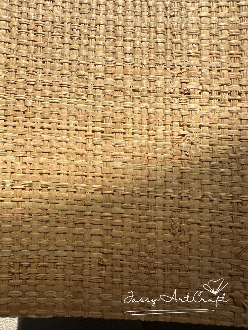 May include: Close-up of a woven material with a natural, light brown color. The texture is created by a tight, repeating pattern of interwoven strands. The weave appears sturdy and the overall effect is rustic and organic.