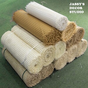 May include: A stack of rolled upholstery webbing in various colors, including white, beige, and brown. The webbing is a woven material used for supporting furniture cushions.