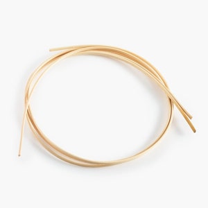 May include: A close-up of a bundle of natural, light brown, flexible, round, wooden dowels. The dowels are arranged in a circle.