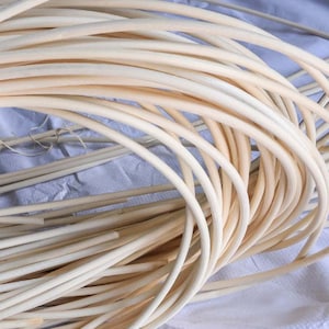 May include: A close-up of a bundle of natural, unpainted, light brown, flexible, round, wooden rods. The rods are approximately 1/2 inch in diameter and are used for weaving baskets or other crafts.