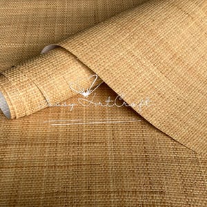 May include: A roll of natural-toned woven material, possibly wallpaper or fabric, with a textured surface. The material is partially rolled, revealing a white backing. The image has a warm, neutral color palette.