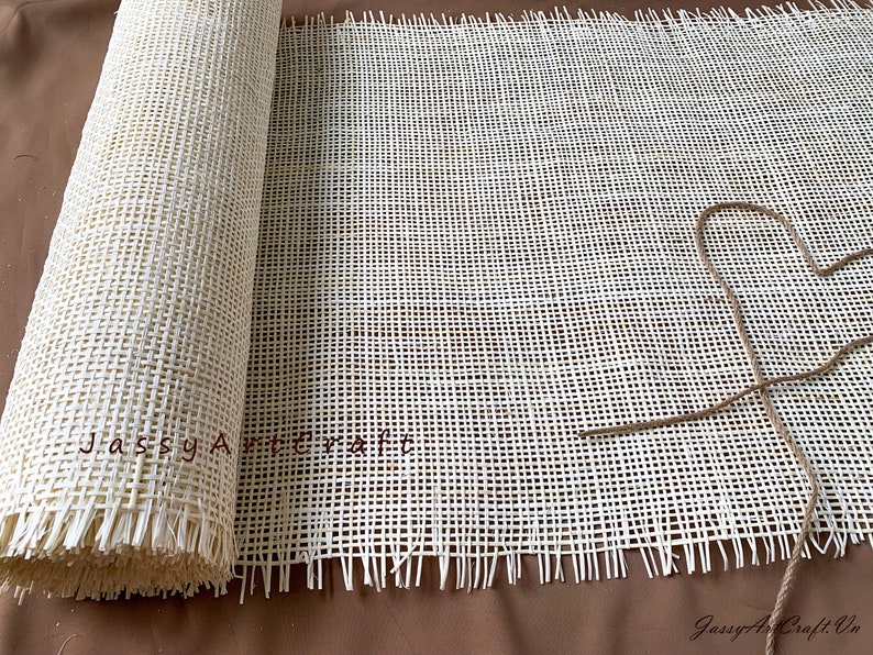 Puede incluir: Un rollo de tejido de ca&ntilde;a blanco tejido con bordes deshilachados. El tejido est&aacute; enrollado y atado con una cuerda. El texto "Jassy Artcraft" est&aacute; impreso en el tejido.