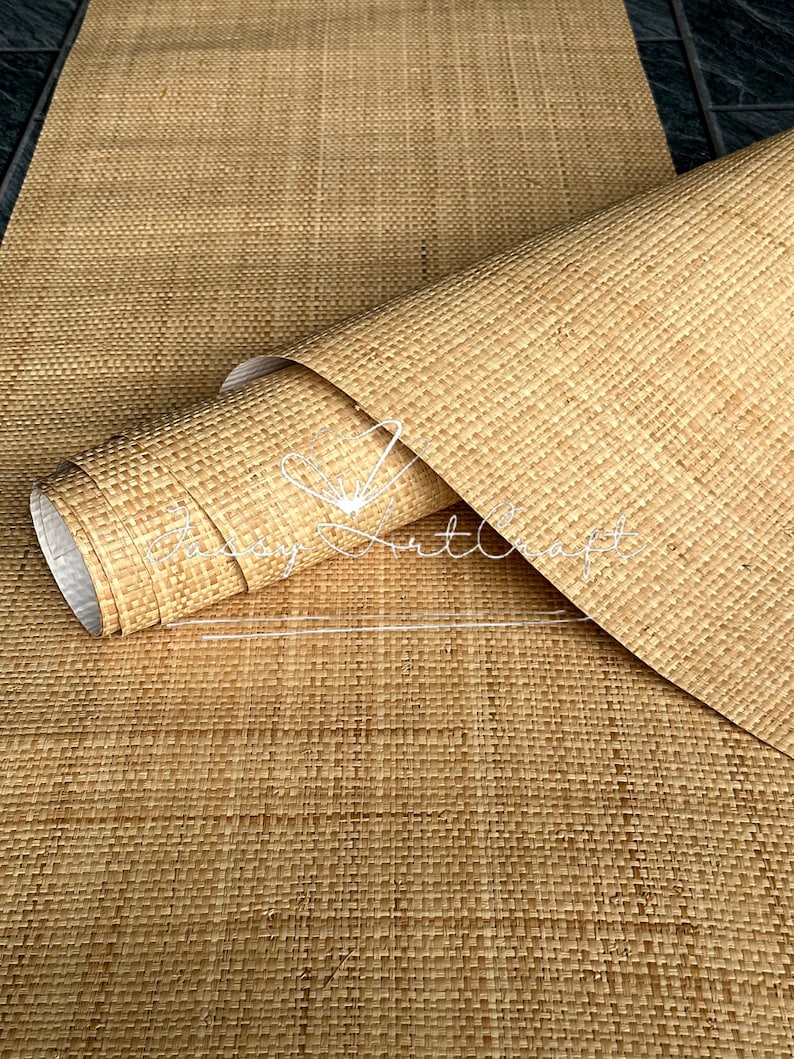 May include: A rolled-up, woven, tan-colored mat with a textured surface. The mat is made of natural fibers and appears to be a runner or placemat. The image shows the mat partially unrolled, revealing the rolled portion.