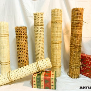 Puede incluir: Cinco rollos de tejido de ca&ntilde;a en varios tama&ntilde;os y colores, incluyendo natural, marr&oacute;n y blanco. Los rollos est&aacute;n atados con cuerda y est&aacute;n dispuestos sobre una superficie blanca.