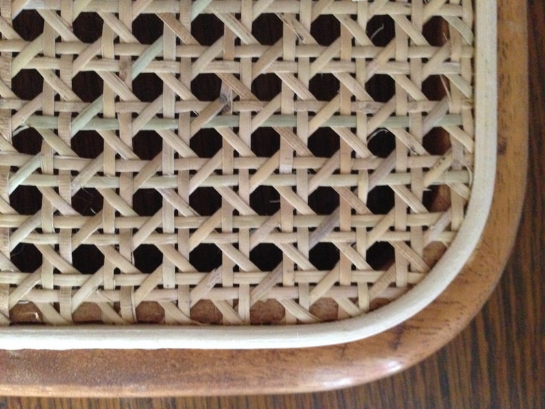 May include: Close-up of a woven cane seat with a white border and a brown wooden frame.