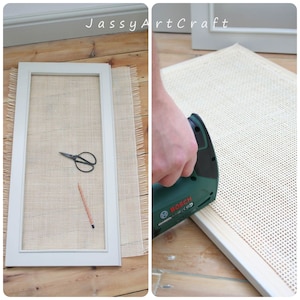 May include: A close-up of a person using a green power stapler to attach a beige mesh fabric to a white wooden frame. The fabric has a fringe edge. The frame is on a wooden floor.