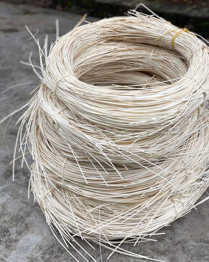 May include: A large bundle of white, woven rattan, tightly wound into a coil. The rattan is used for crafting furniture and other items.