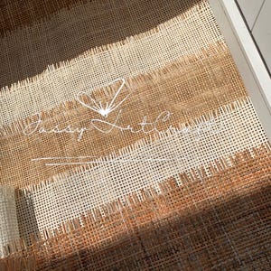 May include: Close-up of woven material in shades of brown and cream, arranged in horizontal stripes. The material has a textured, open weave. The text "Jassy Art Concepts" is visible in white script. The material appears to be inside a white drawer.