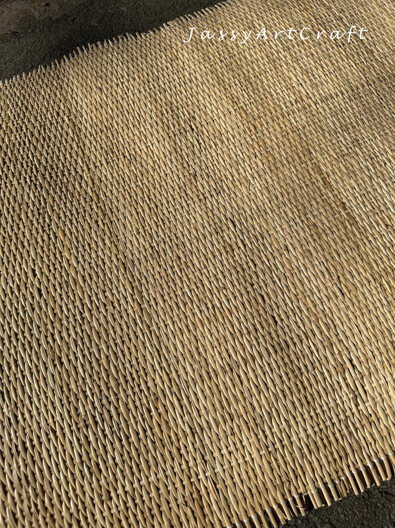 Pode incluir: Um close-up de um tapete natural tecido de palha ou juncos. O tapete tem uma cor castanho claro e uma superf&iacute;cie texturizada. O tapete &eacute; tecido em um padr&atilde;o apertado, criando uma superf&iacute;cie lisa e uniforme.