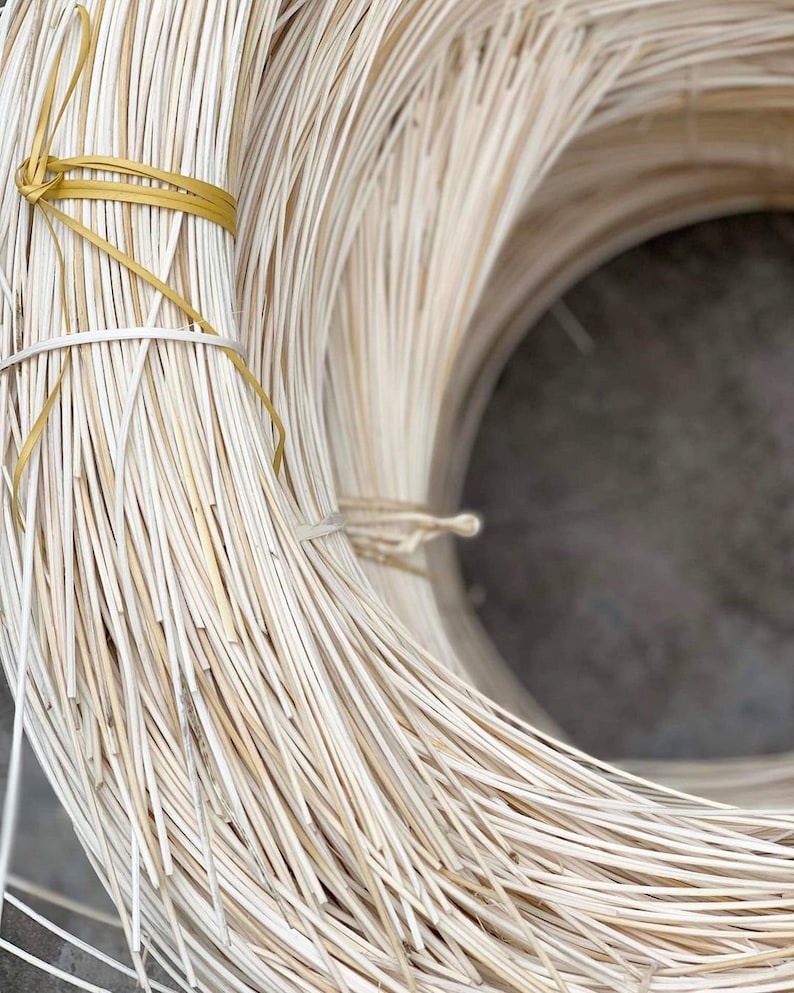 May include: A close-up of a large roll of white, woven rattan, tied with a yellow ribbon. The rattan is used for crafting furniture and other items.