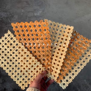 May include: Several woven rattan placemats in varying shades of tan and orange are displayed. The placemats have a geometric pattern of intersecting lines and circular openings. The text "Tossy Art Craft" is visible in the image.
