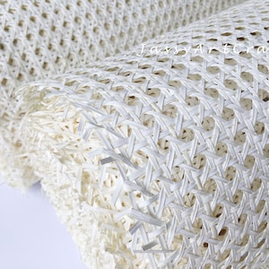 May include: Close-up of a rolled-up, off-white woven material. The material has a repeating pattern of interwoven strips, creating a grid-like texture with open spaces. The texture is visible, and the material appears to be flexible.