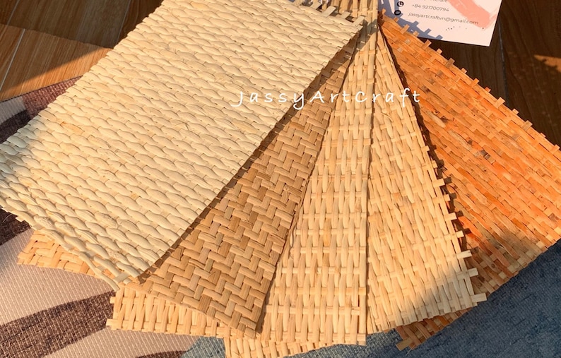 May include: A collection of woven placemats in various natural tones, including light beige, tan, and orange. The mats feature different textures and patterns, showcasing the craftsmanship of the weaving. The image includes the text "JassyArtCraft".
