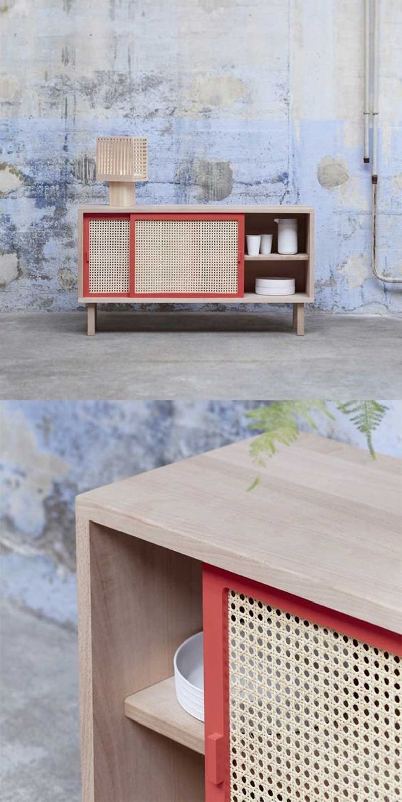 May include: A light wood cabinet with a red-framed, woven cane sliding door. The cabinet has a shelf and is topped with a small, beige lamp. The cabinet is on short legs and has a minimalist design. The background is a textured wall.