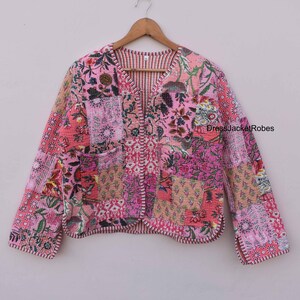 May include: A pink quilted jacket with a floral patchwork design. The jacket has a V-neck and long sleeves. The fabric is soft and comfortable.