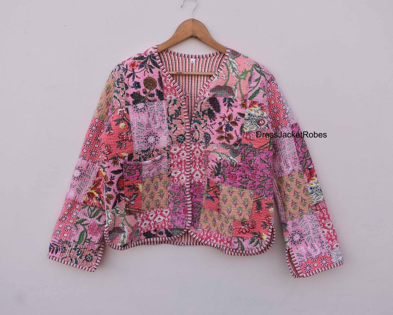 May include: A pink quilted jacket with a floral patchwork design. The jacket has a V-neck and long sleeves. The fabric is soft and comfortable.