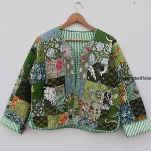 May include: A green patchwork jacket with a floral print. The jacket has a V-neck and a button closure. The sleeves are long and have a striped trim.