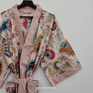 Pode incluir: Robe rosa claro com padrão floral e acabamentos listrados, pendurado em um cabide preto. O robe apresenta um cinto de amarrar e o texto "DressJacketRobes". O design floral inclui detalhes azuis, amarelos e vermelhos.