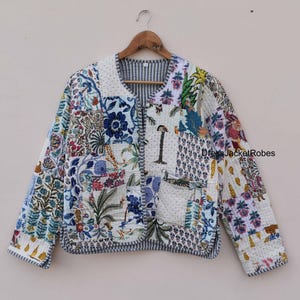 May include: A white quilted jacket with a patchwork design featuring floral and geometric patterns in shades of blue, green, and pink. The jacket has a button closure and a pocket on the left side.