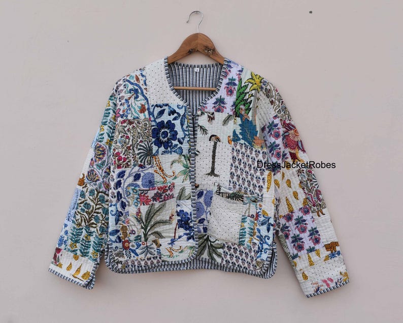 May include: A white quilted jacket with a patchwork design featuring floral and geometric patterns in shades of blue, green, and pink. The jacket has a button closure and a pocket on the left side.