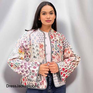 May include: A white quilted jacket with a floral print and black trim. The jacket has a button closure and long sleeves.