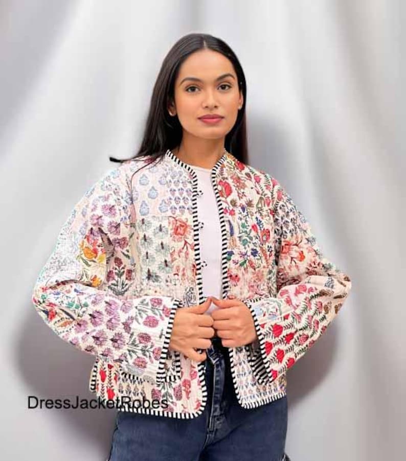 May include: A white quilted jacket with a floral print and black trim. The jacket has a button closure and long sleeves.