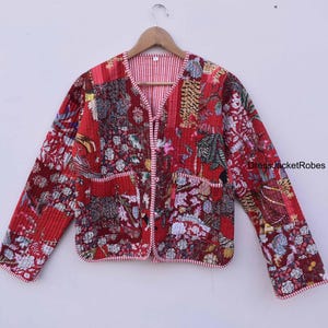 May include: Red quilted jacket with a floral print and a white and red striped lining. The jacket has a V-neck and a button closure. DressJacketRobes is printed on the right sleeve.