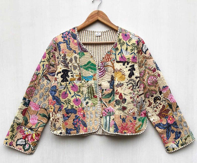 May include: A cream-colored quilted jacket with a floral print. The jacket has a V-neck and long sleeves. The fabric is a patchwork of different floral patterns in shades of pink, blue, green, and yellow.