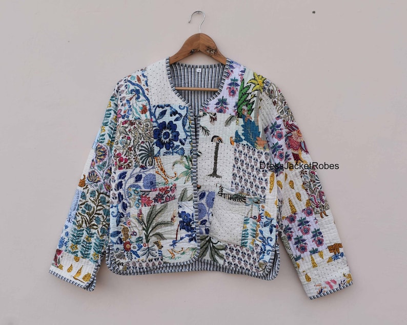 May include: A white quilted jacket with a patchwork design featuring floral and geometric patterns in shades of blue, green, and pink. The jacket has a button closure and a pocket on the left side.
