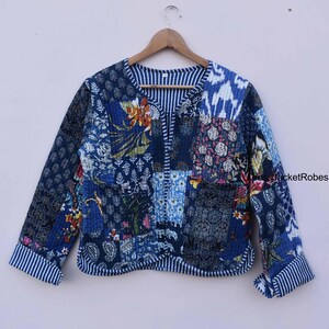 May include: A blue quilted jacket with a patchwork design featuring floral and geometric patterns. The jacket has a V-neck and long sleeves with white stripes on the cuffs.