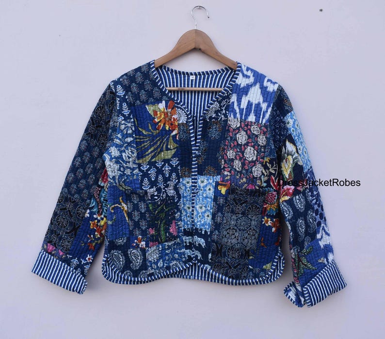 May include: A blue quilted jacket with a patchwork design featuring floral and geometric patterns. The jacket has a V-neck and long sleeves with white stripes on the cuffs.