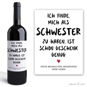 Könnte beinhalten: Eine Flasche Rotwein mit einem weißen Etikett und schwarzem Text. Auf dem Etikett und einer passenden Karte steht "ICH FINDE, MICH ALS SCHWESTER ZU HABEN, IST SCHON GESCHENK GENUG." Die Karte hat auch ein rotes Herz.