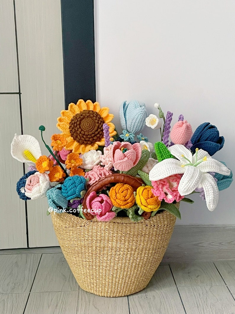 Op de afbeelding: Een gehaakt boeket bloemen in een rieten mand. Het boeket bevat zonnebloemen, lelies, tulpen en andere bloemen in verschillende kleuren.