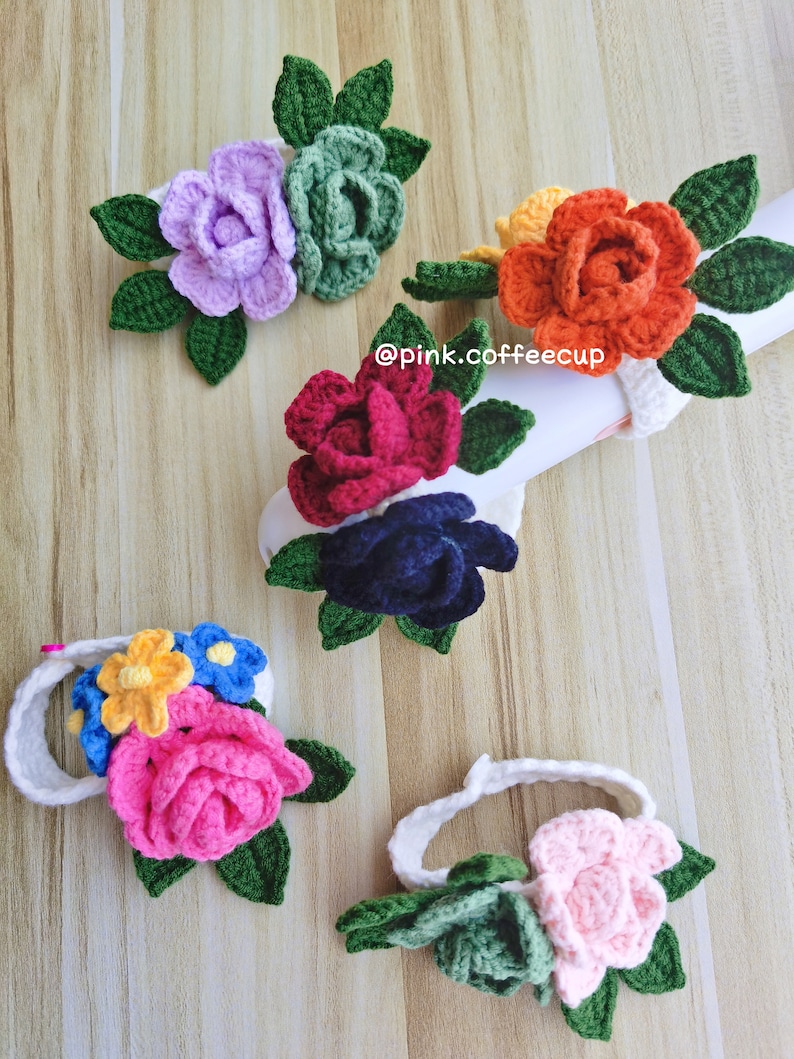 Op de afbeelding: Vijf gehaakte bloemenhaarbandjes in verschillende kleuren, waaronder roze, rood, paars, oranje en wit. Elk haarbandje is versierd met een gehaakte bloem met groene bladeren.