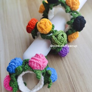 Op de afbeelding: Twee gebreide bloemen haarbandjes. De eerste haarband heeft zwarte, gele, oranje, groene en paarse bloemen. De tweede haarband heeft roze, blauwe en groene bloemen. De haarbandjes liggen op een witte achtergrond met de tekst "@pink.coffeecup".
