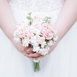 Op de afbeelding: Een gehaakt bruidsboeket met roze en witte bloemen en groene bladeren.