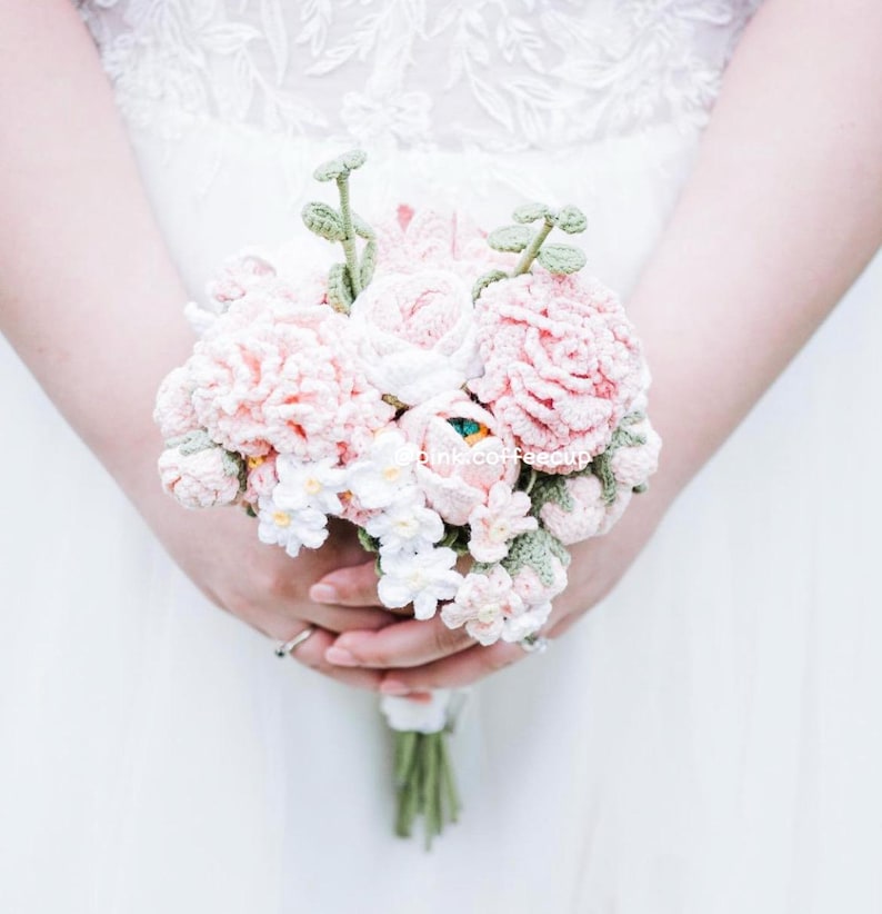 Op de afbeelding: Een gehaakt bruidsboeket met roze en witte bloemen en groene bladeren.