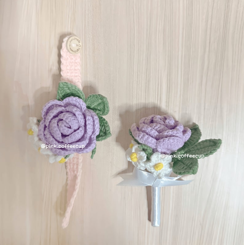 Op de afbeelding: Twee gehaakte bloemboeketten, een met een roze band, beide met paarse rozen en witte madeliefjes. De boeketten zijn op een lichte houten achtergrond.