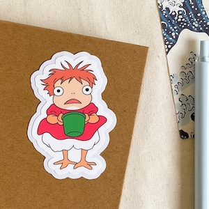 May include: A white sticker featuring a cartoon illustration of a red-haired girl holding a green cup. She is wearing a red dress and has large eyes.