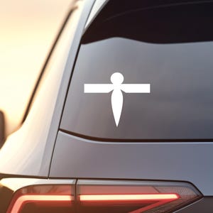 May include: White vinyl decal of a stylized dragonfly with a long, pointed body and spread wings. The decal is applied to the rear window of a black car.