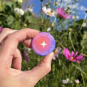 Puede incluir: Una chapa redonda con un degradado vibrante de naranja a morado. El centro muestra un icono de estrella blanca de cuatro puntas. El texto "THINGS ARE FIGURE-OUT-ABLE" está impreso en letras mayúsculas blancas alrededor del borde.