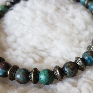May include: A turquoise and brown beaded bracelet with gold accents. The beads are round and have a mottled pattern.