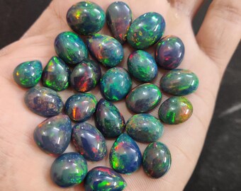 May include: A collection of pear-shaped black opals with green, blue, and red iridescent flashes. The opals are loose and ready to be set in jewelry.