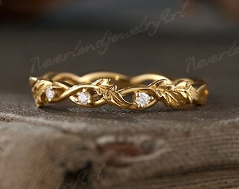 May include: A gold ring featuring a delicate vine and leaf motif that wraps around the band. The design incorporates three small, clear, round-cut stones set at intervals within the metal foliage, creating a continuous, nature-inspired pattern.