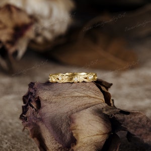 Puede incluir: Una delicada banda de oro con un dise&ntilde;o floral y peque&ntilde;os diamantes. El anillo est&aacute; colocado sobre una rosa seca.