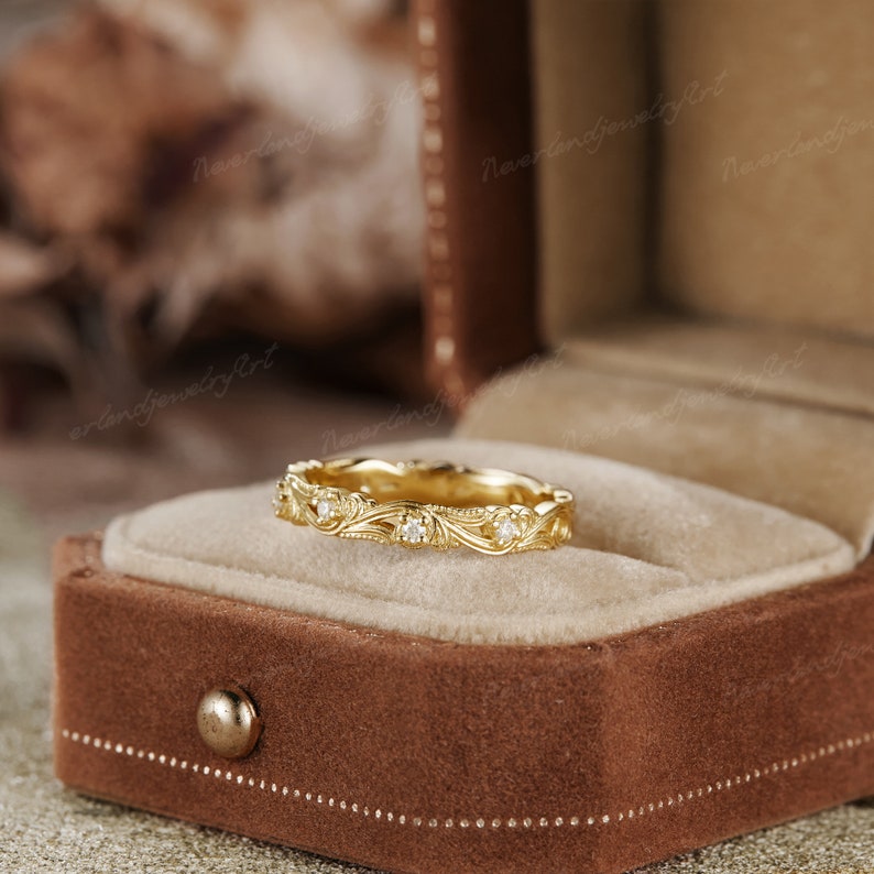 Puede incluir: Una delicada banda de oro con un dise&ntilde;o floral y peque&ntilde;os diamantes. El anillo est&aacute; en una caja de anillo de terciopelo marr&oacute;n.