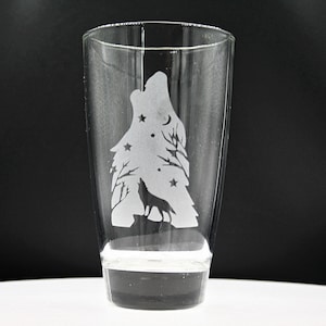 Puede incluir: Un vaso de vidrio transparente con un diseño esmerilado de un lobo aullando a la luna con estrellas en el fondo.